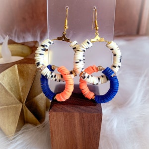 May include: A pair of hoop earrings with a layered design. The hoops are made of white, black, and orange beads. The earrings are hanging from gold hooks.