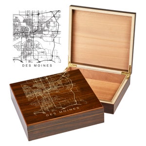 May include: A wooden cigar box with a gold engraved map of Des Moines, Iowa on the lid. The box is closed, but the lid is open to show the interior.