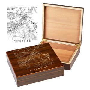 May include: A wooden box with a hinged lid. The lid is open and the inside of the box is lined with wood. The box is decorated with a map of Riverside, California. The text "Riverside" is printed on the box.