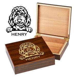 May include: A wooden box with a hinged lid. The lid is open and the inside of the box is visible. The box is decorated with a gold-colored engraving of a dog's head and the name "HENRY".