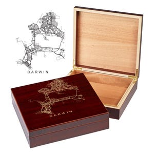 May include: A wooden box with a hinged lid. The top of the box is a dark red colour and features a gold-coloured map of Darwin, Australia. The lid is made of light wood and is open to reveal the interior of the box.