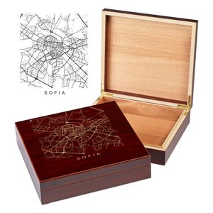 May include: A wooden box with a hinged lid. The top of the box is a dark red color and features a gold-colored map of Sofia, Bulgaria. The lid is made of light wood and is open to reveal the interior of the box.