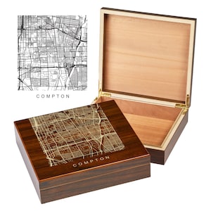 May include: A wooden cigar box with a hinged lid. The top of the box features a laser-engraved map of Compton, California. The city name is also engraved on the box.