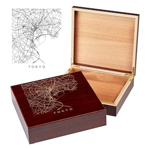 May include: A wooden box with a hinged lid. The top of the box is a dark red mahogany color and features a gold engraved map of Tokyo. The inside of the box is lined with a light wood. The box is closed in the image.