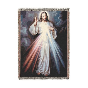 May include: A woven throw blanket featuring the Divine Mercy image of Jesus Christ. The design displays a figure in white robes with rays of red and blue light emanating from the chest against a dark background, finished with a fringed edge.