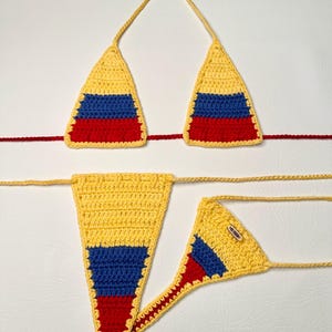 Puede incluir: Un top y una parte inferior de bikini de crochet amarillo, azul y rojo. El bikini está diseñado en los colores de la bandera colombiana.