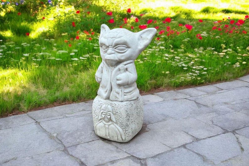以下が含まれることがあります： スターウォーズのヨーダの白いコンクリート像が、ダース・ベイダーの彫刻が施された台座の上に立っています。像は石畳の屋外にあります。
