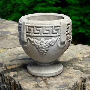 May include: A gray concrete planter with a Greek key design and grapevine motif. The planter has a round body and a pedestal base.