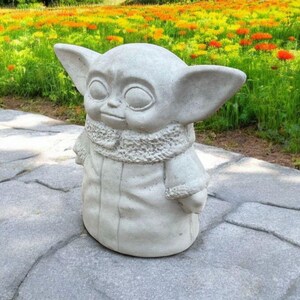 Pu&ograve; includere: Una statua di cemento grigio di un personaggio immaginario con grandi orecchie, che indossa una tunica con cappuccio. La statua &egrave; in piedi su un sentiero di pietra grigia.