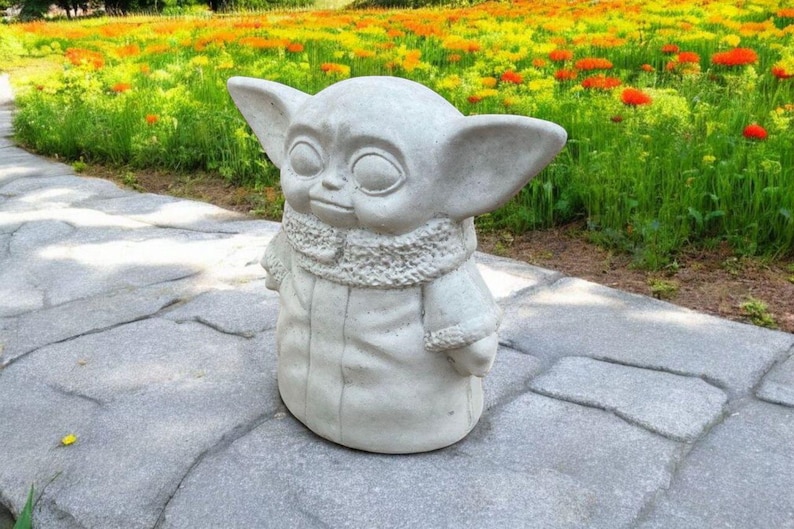 Pu&ograve; includere: Una statua di cemento grigio di un personaggio immaginario con grandi orecchie, che indossa una tunica con cappuccio. La statua &egrave; in piedi su un sentiero di pietra grigia.