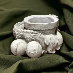 May include: A white ceramic planter shaped like a baseball glove holding two baseballs. The planter is designed to hold a small plant or succulent.