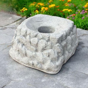 May include: A gray concrete planter with a rough, textured surface. The planter has a circular opening in the center.
