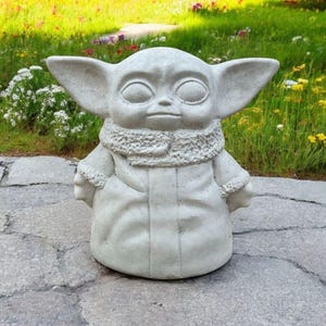 Pu&ograve; includere: Una statua di cemento grigio di un personaggio immaginario del franchise di Star Wars. Il personaggio indossa una tunica con cappuccio marrone e ha grandi orecchie.