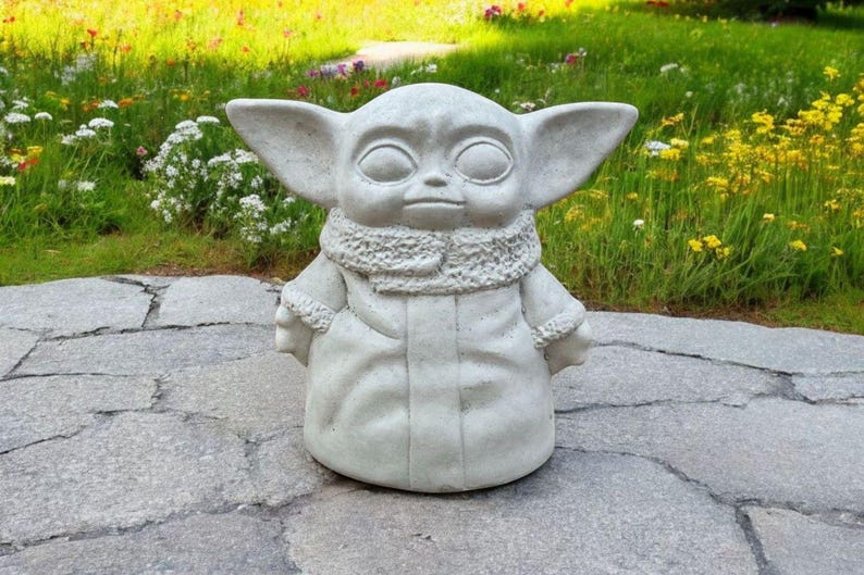 Pu&ograve; includere: Una statua di cemento grigio di un personaggio immaginario del franchise di Star Wars. Il personaggio indossa una tunica con cappuccio marrone e ha grandi orecchie.