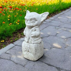 以下が含まれることがあります： スターウォーズのフランチャイズのキャラクター、ヨーダの白いコンクリート像が、ダース・ベイダーを描いた台座の上に立っています。像は灰色の石の歩道の上にあります。