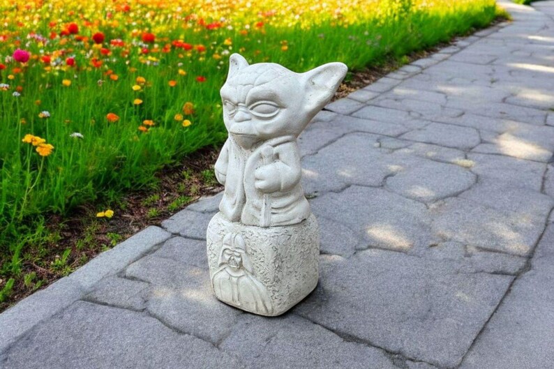 以下が含まれることがあります： スターウォーズのフランチャイズのキャラクター、ヨーダの白いコンクリート像が、ダース・ベイダーを描いた台座の上に立っています。像は灰色の石の歩道の上にあります。