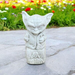 以下が含まれることがあります： スターウォーズのヨーダの白いセラミック像。ヨーダは茶色のローブを着ており、顔には真剣な表情をしています。彼はダース・ベイダーを描いた台座の上に立っています。