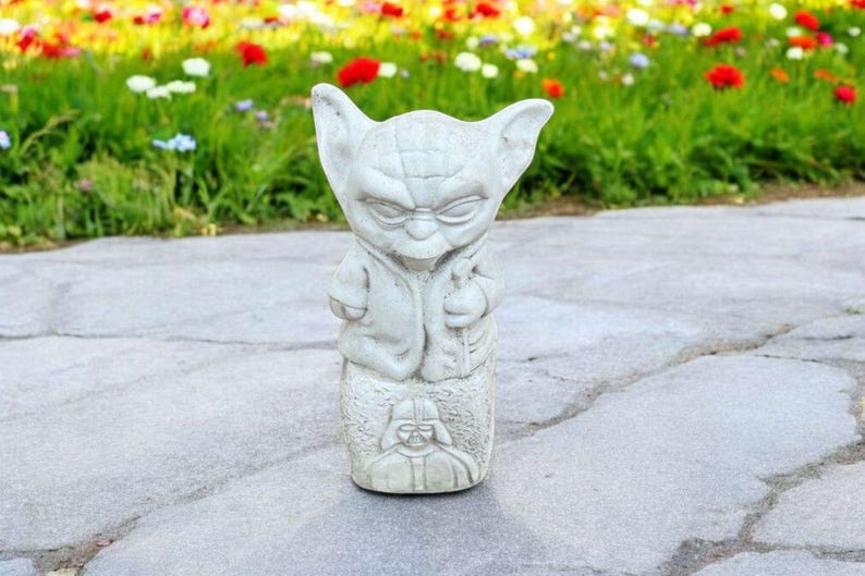 以下が含まれることがあります： スターウォーズのヨーダの白いセラミック像。ヨーダは茶色のローブを着ており、顔には真剣な表情をしています。彼はダース・ベイダーを描いた台座の上に立っています。