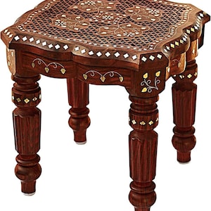 May include: A square wooden stool with a dark brown finish, featuring intricate brass inlay patterns on the top surface and apron. The stool stands on four carved, turned legs with matching brass accents and a lattice design on the top.
