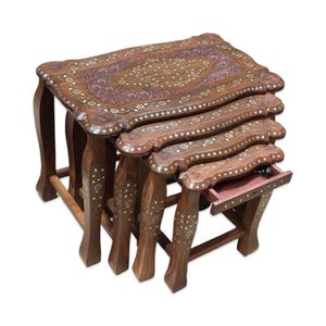 May include: A set of four wooden nesting tables with intricate floral inlay designs. The tables are various sizes, with curved legs and a warm brown finish. One table has a small drawer. The largest table is approximately 24 inches long.
