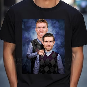 May include: A black t-shirt with a graphic print of two men wearing sweaters. The men are standing next to each other and have a blue and gray background.