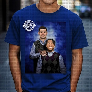 Puede incluir: Camiseta azul real con una imagen impresa de dos hombres con chalecos de rombos y camisas con cuello sobre un fondo azul. La camiseta también tiene un gráfico circular que dice "100% Original Design".