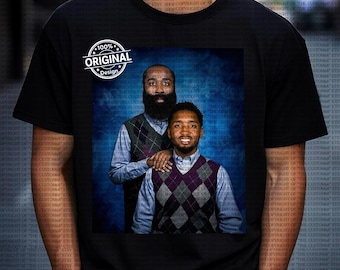 Op de afbeelding: Zwart T-shirt met een portret van twee mannen in ruitjesvesten en overhemden met knopen tegen een blauwe achtergrond. Het shirt heeft ook een cirkelvormig "100% Original Design" logo.