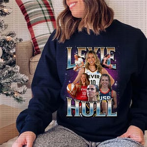 Pode incluir: Uma camisa de moletom azul marinho com uma estampa gráfica da jogadora de basquete Lexie Hull. O gráfico apresenta uma colagem de imagens de Hull jogando basquete, incluindo um close-up de seu rosto e uma foto dela driblando a bola. O texto "Lexie Hull" é impresso em letras grandes e em negrito na frente da camisa de moletom.