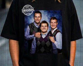 Op de afbeelding: Zwart T-shirt met een afbeelding van drie mannen in argyle vesten en overhemden met kraag. De afbeelding is omlijst door een witte cirkel met de tekst "100% ORIGINAL Design".