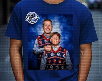 Op de afbeelding: Koningsblauw T-shirt met een afbeelding van twee mannen in bijpassende blauwe, rode en witgepatroneerde vesten. De afbeelding bevat de tekst "100% ORIGINAL Design" in een cirkelvormige badge.