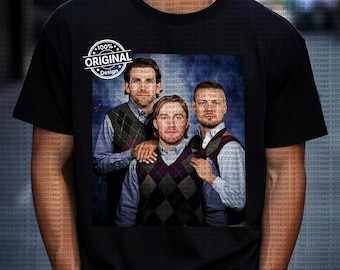 Op de afbeelding: Zwart T-shirt met een groepsportret van drie mannen in argyle vesten en overhemden met knopen. De afbeelding heeft een blauwe achtergrond. Het shirt heeft ook een cirkelvormig "100% Original Design" logo.