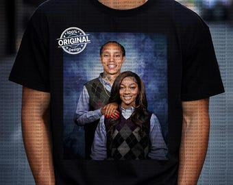 Op de afbeelding: Zwart T-shirt met een portret van twee mensen, waarvan één met een arm om de ander. Ze dragen argyle vesten over overhemden met kraag. Het shirt heeft een "100% Original Design" logo.