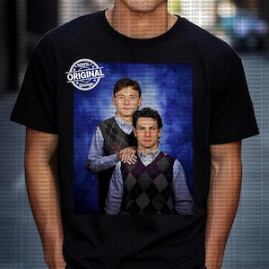 May include: Black t-shirt with a printed image of two men in argyle vests and collared shirts against a blue background. The shirt also has a white circular design with the text "100% ORIGINAL Design."