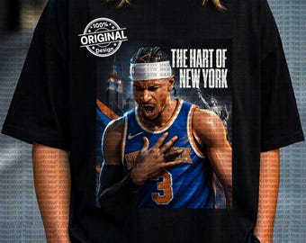 Op de afbeelding: Zwart T-shirt met een afbeelding van een basketballer in een blauw en oranje uniform, met de tekst "THE HART OF NEW YORK." Het ontwerp bevat de tekst "100% ORIGINAL Design."