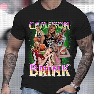 Pode incluir: Uma camiseta preta com uma estampa gráfica de jogadoras de basquete. O texto "CAMERON BRINK" está impresso em letras rosa e amarelas na camiseta.