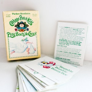 May include: A vintage Cabbage Patch Kids card game box and cards. The box is light yellow with the words "Cabbage Patch Kids" and "Ptits Bouts de Choux". The cards feature illustrations of characters and the text "Stumble Bumble Bunny Bee".