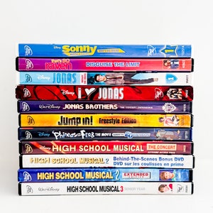 Może przedstawiać: Stos 10 pudełek DVD z różnymi programami i filmami Disney Channel, w tym Sonny z szansą, To takie Raven, Jonas, Jump In!, Phineas i Ferb oraz High School Musical. Pudełka są ułożone pionowo, z tytułami skierowanymi do przodu.