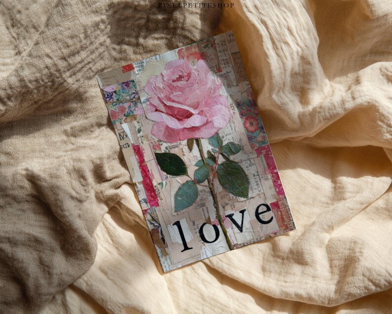 May include: A rectangular card featuring a pink rose with green leaves and the word "love" in black. The card has a collage-like background with floral and text elements. The card is set against a beige, textured fabric.