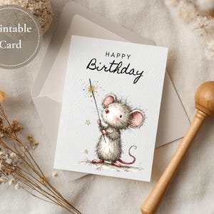 May include: A printable birthday card featuring a watercolor illustration of a cute mouse holding a sparkler. The card reads "Happy Birthday" in elegant script. The card is inside a white envelope, with a wooden rattle and dried flowers nearby.