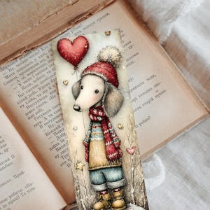 May include: A whimsical bookmark featuring a dachshund wearing a red hat and scarf, holding a heart-shaped balloon. The illustration has a winter theme with a soft, muted color palette and a vintage book background.