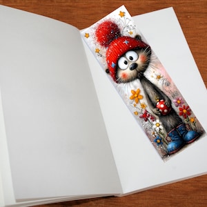 May include: A colourful bookmark depicting a cartoon cat in a red hat and blue boots, holding a polka-dot bauble. The cat is surrounded by flowers. The bookmark is placed in an open book, with the pages visible.