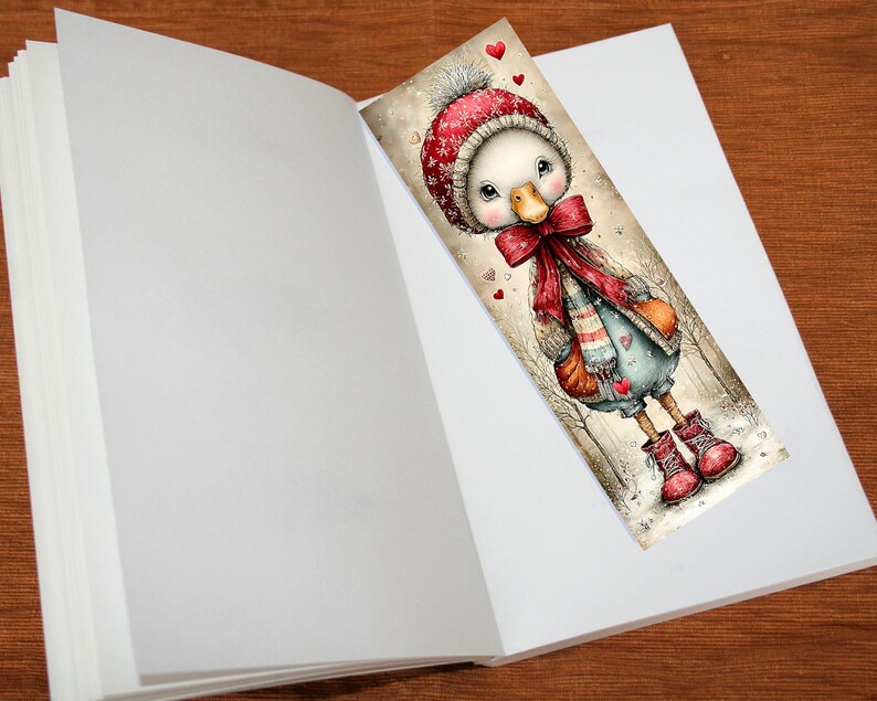 May include: A whimsical bookmark featuring a cartoon duck wearing a red winter hat, scarf, and boots. The duck is standing in a snowy scene with hearts. The bookmark is placed inside an open book.