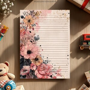 May include: Lined stationery with a floral design featuring pink and peach flowers. The stationery has a watercolor effect with gold accents. The image also includes a teddy bear, a toy train, and a wrapped gift.
