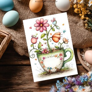 May include: A greeting card with a whimsical illustration of flowers growing from a teacup. The flowers are pink and orange, with green leaves and stems. The teacup is white with a green handle and is decorated with small flowers. The background is a wooden table.