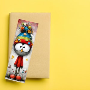 May include: A colourful bookmark depicting a cartoon owl with big eyes, wearing a hat decorated with stars and buttons, and a red outfit. The bookmark rests on a brown book against a yellow background.