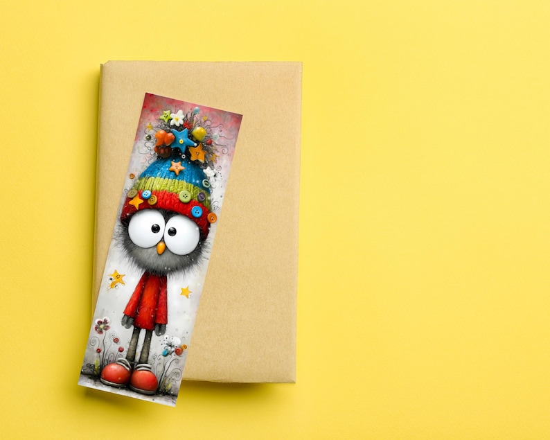 May include: A colourful bookmark depicting a cartoon owl with big eyes, wearing a hat decorated with stars and buttons, and a red outfit. The bookmark rests on a brown book against a yellow background.