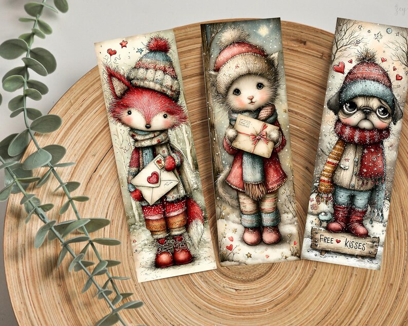 May include: Three whimsical bookmarks featuring winter-themed animal characters. A fox, cat, and pug are depicted in cozy winter attire, holding letters or wearing scarves. The pug bookmark has the text "FREE KISSES" on a small wooden sign.