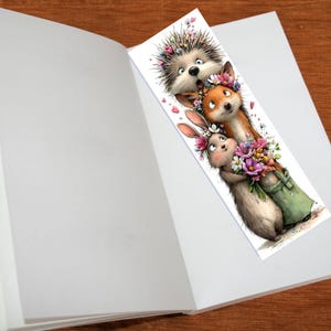 May include: A whimsical bookmark featuring a hedgehog, fox, and rabbit, each adorned with floral crowns. The rabbit holds a bouquet of flowers in a green bag. The bookmark is placed inside an open book.