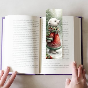 Puede incluir: Un marcap&aacute;ginas caprichoso con un oso polar con un abrigo rojo con adornos verdes y una corona festiva. La ilustraci&oacute;n est&aacute; ambientada sobre un fondo nevado, a&ntilde;adiendo un toque de encanto invernal. El marcap&aacute;ginas est&aacute; en un libro abierto.