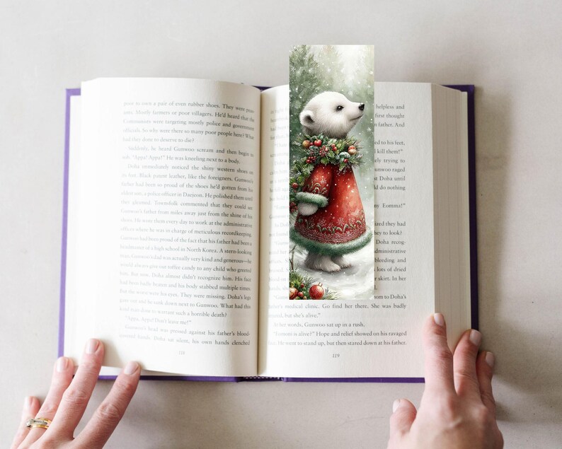 Puede incluir: Un marcap&aacute;ginas caprichoso con un oso polar con un abrigo rojo con adornos verdes y una corona festiva. La ilustraci&oacute;n est&aacute; ambientada sobre un fondo nevado, a&ntilde;adiendo un toque de encanto invernal. El marcap&aacute;ginas est&aacute; en un libro abierto.